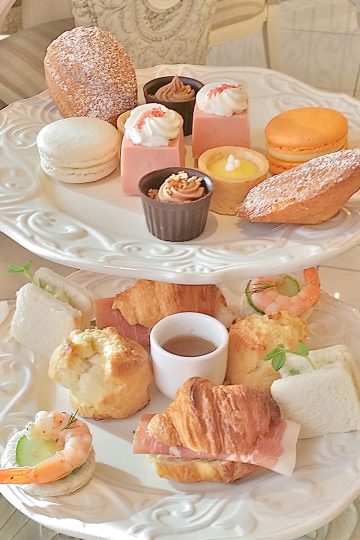 A 2-tier afternoon tea display featuring little cute treats in pastel colors and little croissant sandwiches.