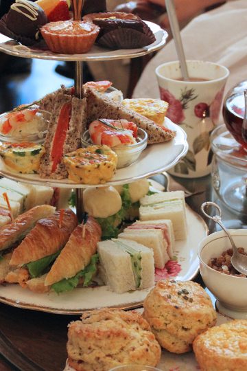 Afternoon tea set shown with a pot of tea in a glass kettle alongside some scones, vintage tea cups and a bowl of sugar.