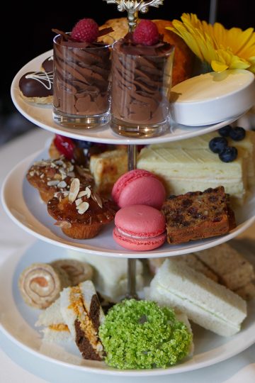 A traditional afternoon tea set on a 3-tier-tray filled with chocolate mousse, macarons, financiers and mini sandwiches.