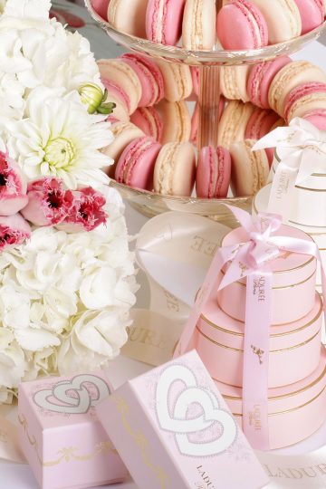 A beautiful assortment of macaron boxes assembled on a tabletop adorned with fresh flowers and a macaron tower.