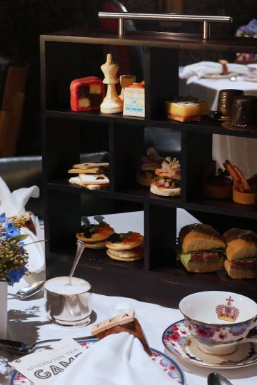 A square shaped afternoon tea display set on a table with a bone china tea set in the front of it.
