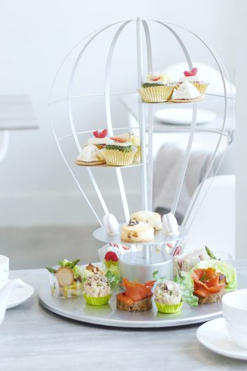 A balloon shaped food display presenting afternoon tea treats on a marble tabletop in a room filled with tons of natural light.