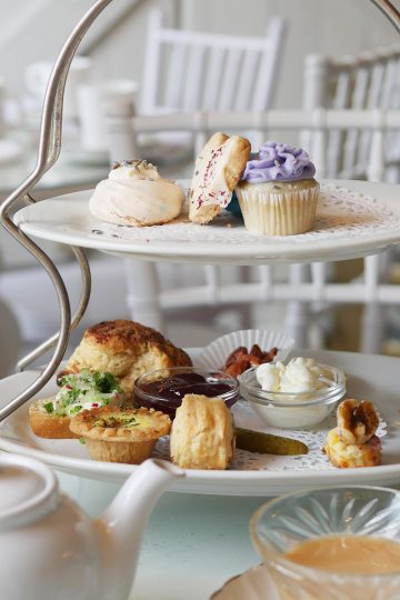 An afternoon tea set on a beautiful white table with lots of white farmhouse furniture in the background.