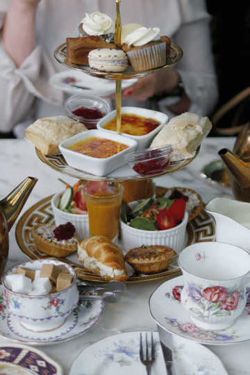 A 3-tier afternoon tea tray with gold accents filled with little treats like macarons, croissants and other tea foods.
