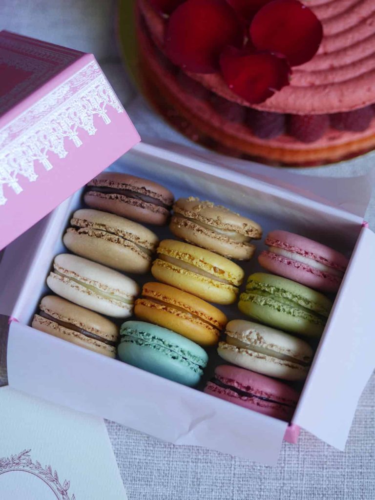 A box of 12 Laduree macarons with a big macaron cake in the back.